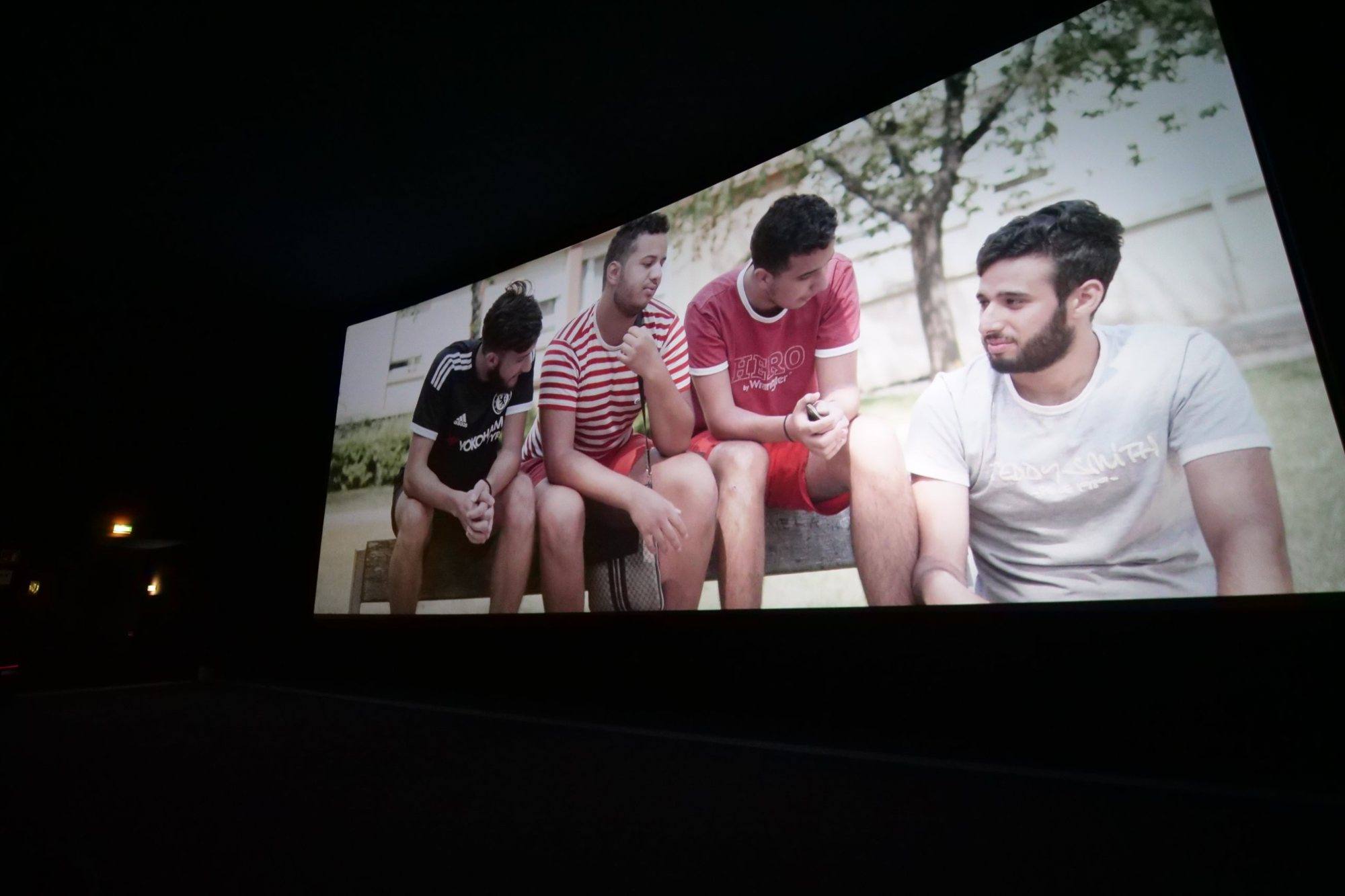 Still from the film: four young men sitting on a bench outside an apartment building